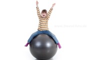 Kind sitzt auf großem Medizin Ball und hat Spaß