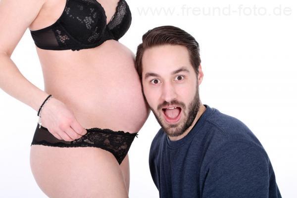 Mann ist überrascht und horcht am Babybauch